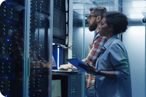 Modern multiethnic man and woman with tablet using laptop in server room while checking servers